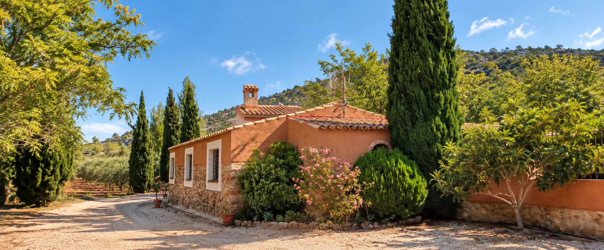 Fachada de la masía rodeada de cipreses y vegetación mediterránea